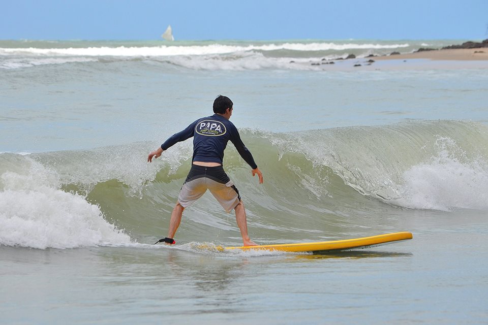 Aluno surfando uma onda com prancha amarela