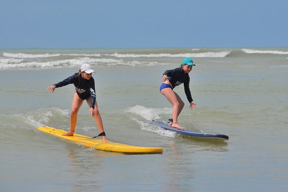 Duas alunas praticando surf lado a lado